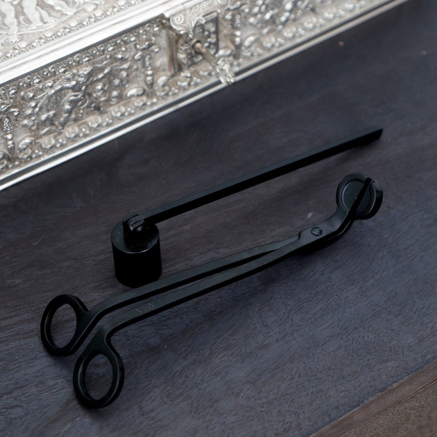 Black candle snuffer beside an ornate silver tray